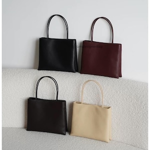 May include: Four rectangular handbags with thin shoulder straps, arranged in a grid. The bags are black, dark burgundy, dark brown, and beige. The text YumDesignerBag is visible on the burgundy bag. Each bag features a smooth, solid-colored exterior.