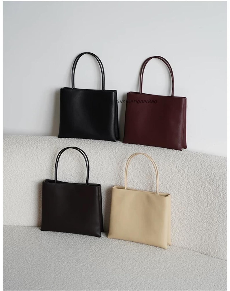 May include: Four rectangular handbags with thin shoulder straps, arranged in a grid. The bags are black, dark burgundy, dark brown, and beige. The text YumDesignerBag is visible on the burgundy bag. Each bag features a smooth, solid-colored exterior.