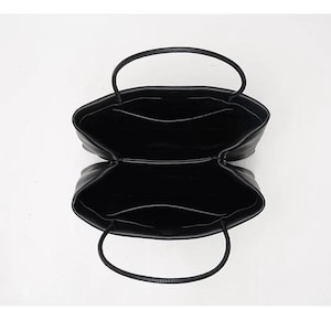 May include: A black handbag viewed from directly above, showing an open interior divided into two main compartments. Each compartment features a flat pocket along the inner wall and a thin, rounded handle extending from the top edge.