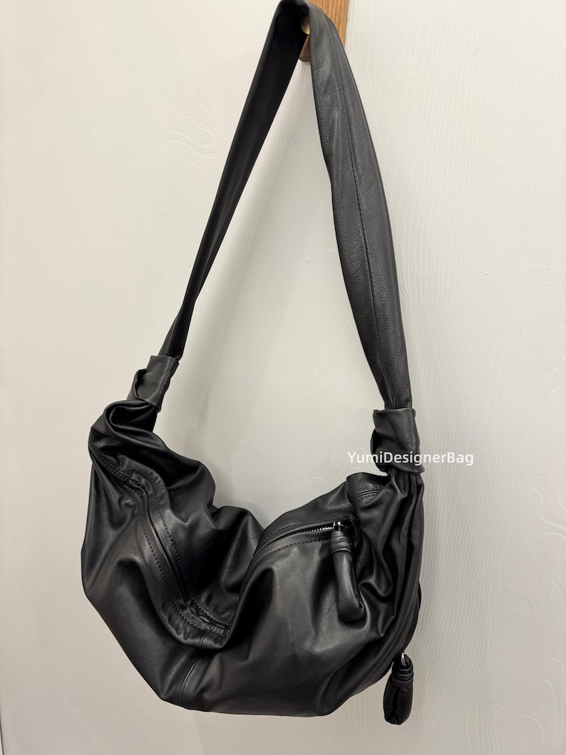 May include: A black leather shoulder bag with a long strap. The bag has a slouchy design with a zipper closure and a tassel detail. The text "YumiDesignerBag" is visible on the right side of the bag.