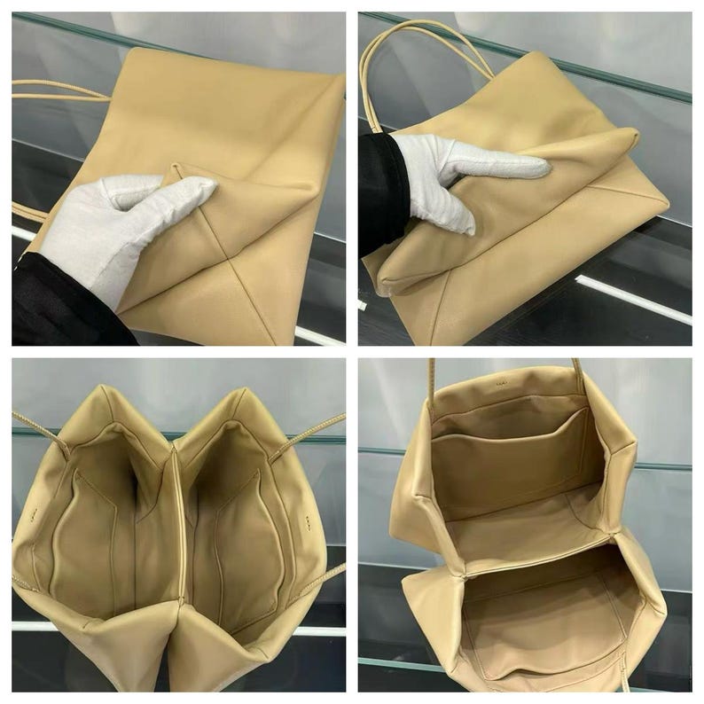 May include: A beige shoulder bag with a smooth finish, featuring thin straps and a structured, multi-compartment interior. The bag has a soft, pliable exterior and includes internal pockets for organization, with a clean, minimalist design throughout.