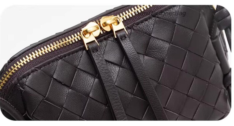 K&ouml;nnte beinhalten: Nahaufnahme einer dunkelbraunen Tasche aus geflochtenem Leder. Die Tasche hat einen goldenen Rei&szlig;verschluss und zwei goldene Rei&szlig;verschlusszipper. Das Leder ist in einem Flechtmuster gewebt. Die Tasche hat zwei Lederriemen, die am Rei&szlig;verschluss befestigt sind.