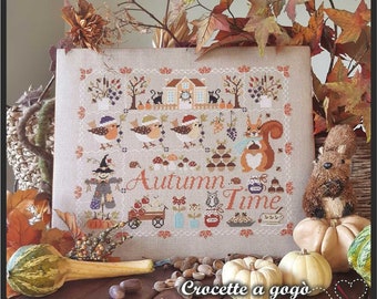 May include: A cross-stitch pattern featuring a whimsical autumn scene with a house, birds, a squirrel, a scarecrow, and the text "Autumn Time". The pattern is framed and surrounded by fall-themed decorations, including gourds, acorns, and leaves.