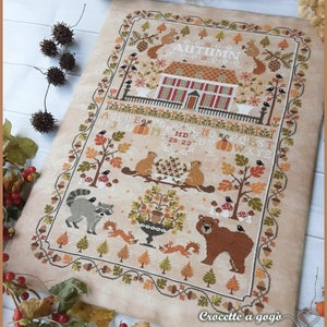 Peut inclure: Mod&egrave;le de point de croix repr&eacute;sentant une charmante sc&egrave;ne d'automne avec une maison, des arbres, des animaux et le mot "AUTUMN". Le motif comprend une vari&eacute;t&eacute; de couleurs, notamment le brun, l'orange, le rouge et le vert.
