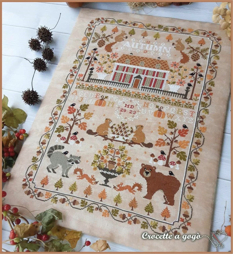 Peut inclure: Mod&egrave;le de point de croix repr&eacute;sentant une charmante sc&egrave;ne d'automne avec une maison, des arbres, des animaux et le mot "AUTUMN". Le motif comprend une vari&eacute;t&eacute; de couleurs, notamment le brun, l'orange, le rouge et le vert.