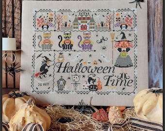 May include: A cross-stitch sampler on beige fabric featuring Halloween motifs including a haunted house, cats, a witch, ghosts, pumpkins, and the text "Halloween Time" and "31 OCT". The design is bordered by a decorative black and white pattern.