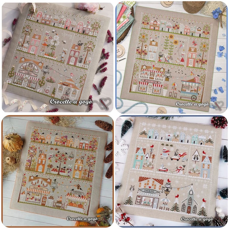 May include: Four cross-stitch patterns depicting a small town with houses, shops, and trees. Each pattern represents a different season: spring, summer, autumn, and winter. The patterns are framed and displayed on a light brown background.