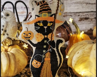 Pode incluir: Um ornamento de tecido bordado em ponto cruz apresentando um gato preto usando um chapéu de bruxa listrado e uma gola laranja. O gato segura uma pequena abóbora em uma pata e uma vassoura na outra, com um balde de abóbora pendurado no braço.