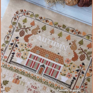 Peut inclure: Mod&egrave;le de point de croix repr&eacute;sentant une charmante sc&egrave;ne d'automne avec une maison, des arbres, des &eacute;cureuils, des oiseaux et des citrouilles. Le motif est intitul&eacute; "Automne" et comprend le texte "Crocette a gogo".