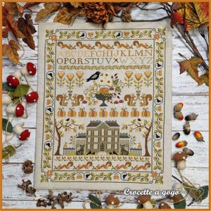 May include: A cross-stitch sampler with an autumnal theme. The design features a house, squirrels, pumpkins, and floral elements. The border includes squirrels and vines. The text "ABC...XYZ" is at the top. The text "Crocette a gogo" is at the bottom.