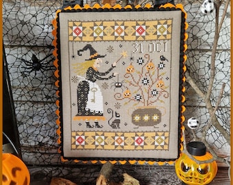 May include: A rectangular cross-stitch embroidery on beige fabric featuring a witch with a wand, a black cat, a spider, and a cauldron. The design includes the text 31 OCT, surrounded by a yellow and black scalloped pom-pom trim border.