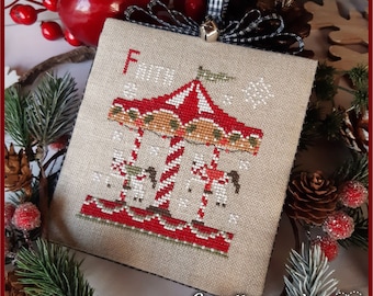 May include: A cross-stitch ornament featuring a red and white striped carousel with two horses and a snowflake design. The ornament is on a beige linen background and has the text "Crocette a gogo" at the bottom.