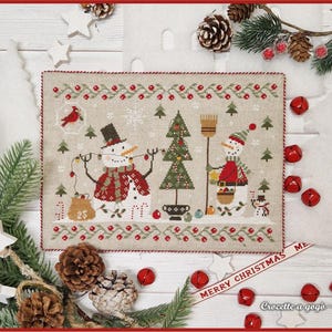 Könnte beinhalten: Eine rechteckige Kreuzstichstickerei auf beigem Stoff mit zwei Schneemännern, einem Weihnachtsbaum und einem Kardinalvogel. Das Design enthält rote Beeren, grüne Tannenbäume und Schneeflocken. Der Rand ist mit einer rot-grünen Beerenranke verziert.
