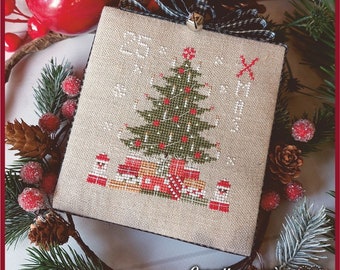 May include: A beige cross-stitch ornament featuring a green Christmas tree with red ornaments and white lights. The tree is surrounded by presents and the text "25" and "XMAS" is stitched above the tree.