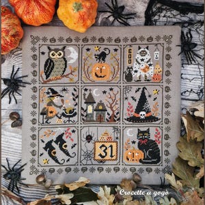 Può includere: Un ricamo a punto croce quadrato su tessuto grigio con nove riquadri distinti a tema Halloween. I disegni includono un gufo, una zucca, un fantasma, una strega, una casa stregata, un cappello da strega, stivali, il numero 31 e un gatto nero con una zucca.