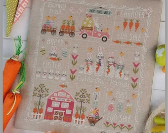 May include: A cross-stitch pattern sampler featuring a bunny trail, carrots for sale, a cottontail family, and a farmhouse with eggs for sale. The sampler is on a beige linen fabric with a white border.