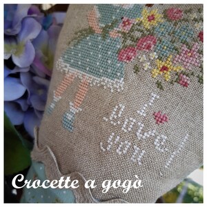 May include: A cross-stitch pattern of a girl in a blue dress holding a bouquet of flowers. The text "Croquette a gogo" is stitched at the bottom of the pattern.
