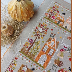 May include: A cross-stitch pattern featuring three houses with orange and brown accents, surrounded by trees, flowers, and a bird. The text "Crochette a gogo" is visible in the bottom right corner.