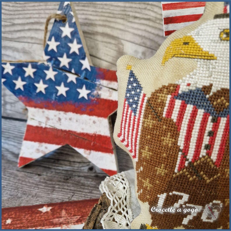 May include: Wooden star and a cross-stitch eagle with American flag details. The star is painted red, white, and blue with a distressed finish. The eagle is cross-stitched with brown, white, and yellow thread, and includes the text "1776".