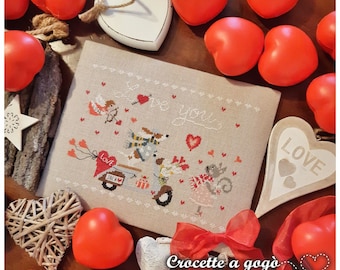 May include: A cross-stitch pattern featuring a dog and a cat riding a scooter with a heart-shaped balloon that says "Love you". The pattern is surrounded by red hearts and a white heart with the word "Love" on it.