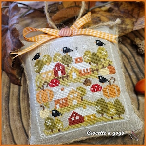 Op de afbeelding: Een kruissteekontwerp met een herfsttafereel met een dorp met rode huizen, pompoenen en bomen. Het ontwerp is omlijst met een jute rand en een decoratief oranje en geel lint. De tekst "Crocette a gog&ograve;" is zichtbaar.