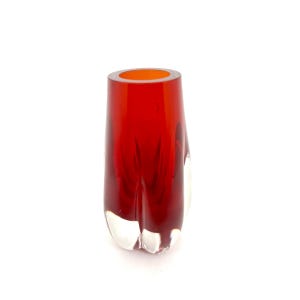 May include: A striking red glass vase with a clear, sculpted base. The vase has a cylindrical shape with a flared opening and a smooth, glossy finish. The interior of the vase is a bright orange colour.