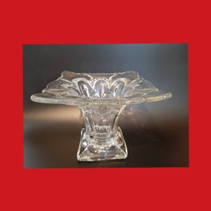 May include: A clear glass vase with a wide, flared opening and a square base. The vase has a delicate, floral design.