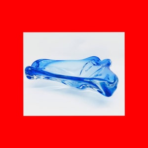 May include: A blue glass bowl with a wavy, organic shape. The bowl is made of clear glass with a blue tint.