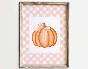 Puede incluir: Una impresión enmarcada de una pintura de acuarela de una calabaza naranja con un lazo rosa sobre un fondo de cuadros rosa y blanco.