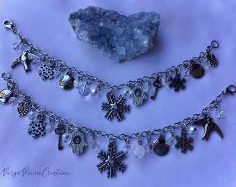 May include: Two silver charm bracelets with various charms, including snowflakes, birds, keys, and beads. One bracelet has an owl charm and the word "Hope". The other has the word "Believe". A blue crystal is in the background.