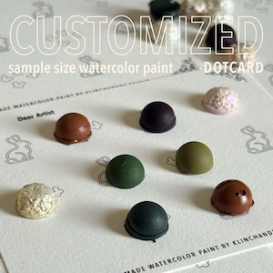 May include: A selection of sample-size watercolour paints in diverse colours, displayed on a white dot card. The card features the words "CUSTOMIZED" and "sample size watercolour paint". The paints are in shades of brown, green, and pink. The card also has a bunny design.