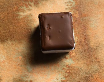 May include: A rectangular watercolor paint pan with a dark brown pigment surface, resting on a square paper swatch featuring a textured, mottled wash of earthy orange and brown tones with the handwritten label 18 Redeyes below it.