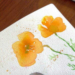 May include: Watercolor painting of two yellow flowers with green stems and leaves on a white background. The flowers are painted in a loose, impressionistic style, with a few splatters of orange paint around them.