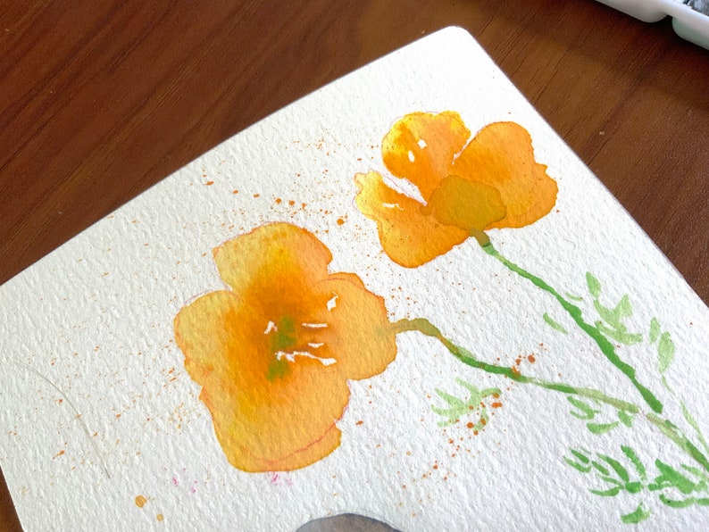 May include: Watercolor painting of two yellow flowers with green stems and leaves on a white background. The flowers are painted in a loose, impressionistic style, with a few splatters of orange paint around them.