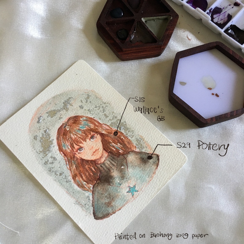 Puede incluir: Pintura acuarela de una ni&ntilde;a con cabello casta&ntilde;o y una estrella azul en su camisa. La pintura est&aacute; sobre un fondo blanco con un efecto de brillo plateado. La pintura est&aacute; firmada "S29 Pottery" y "Sis Wallace's GB".