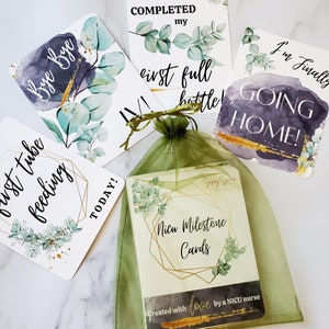 K&ouml;nnte beinhalten: Ein Satz von f&uuml;nf Karten mit Aquarellhintergr&uuml;nden und goldenen Akzenten. Die Karten zeigen Meilensteine f&uuml;r ein Baby auf der Neugeborenenintensivstation, wie z. B. &bdquo;Ich habe meine erste volle Flasche geschafft&ldquo; und &bdquo;Ich gehe endlich nach Hause!&ldquo;. Die Karten sind in einem gr&uuml;nen Organzas&auml;ckchen verpackt mit dem Text &bdquo;NICU Milestone Cards&ldquo; und &bdquo;Created with love by a NICU nurse&ldquo;.