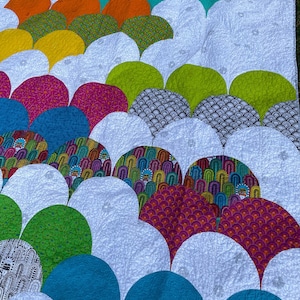 May include: A colorful quilt with a pattern of overlapping semicircles in various colors, including green, blue, pink, yellow, and orange. The quilt is made of fabric with different patterns, including floral, geometric, and abstract designs.