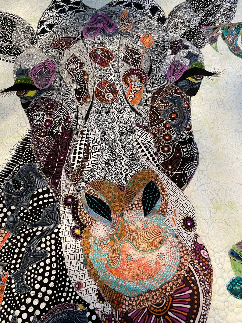May include: Close-up of a colorful, patterned quilt depicting a giraffe's face. The quilt is made of various fabrics and textures, creating a unique and intricate design. The giraffe's eye is large and prominent, with a black and white pattern.