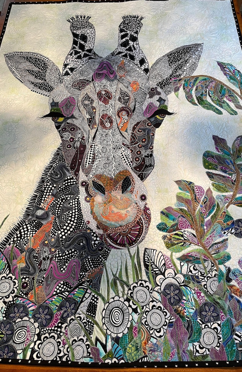 May include: A close-up of a colorful, patterned giraffe quilt. The giraffe's face is prominent, with intricate details in black, white, and purple. The background features a variety of green and purple leaves, as well as black and white flowers.