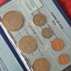 May include: A blue coin collection folder with a clear plastic insert showing a set of uncirculated Fijian coins. The coins are in denominations of 1, 5, 10, 20, and 50 cents. The folder has the text "COINS OF FIJI 1976" printed on the front.