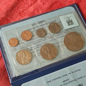 May include: A collection of gold-colored coins in a blue and white display case. The coins feature a profile of Queen Elizabeth II and the text "FIJI COINS 1976".