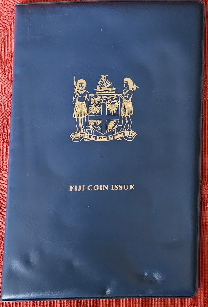 May include: A blue leather coin album with gold lettering that reads "FIJI COIN ISSUE" and a gold crest with two figures and a ship.