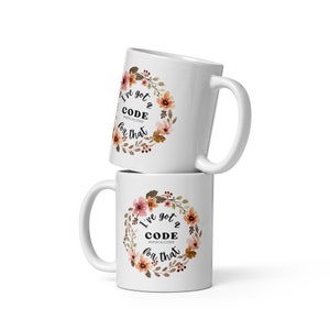 May include: Two white coffee mugs with a floral wreath design. The text on the mugs reads "I've got a CODE for that #MEDICALCODER".