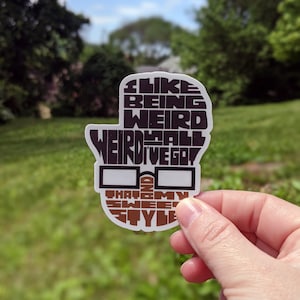 Puede incluir: Una pegatina blanca con texto negro y marrón que dice "Me gusta ser raro, raro es todo lo que tengo y ese es mi estilo dulce". La pegatina tiene un gráfico de un par de gafas.