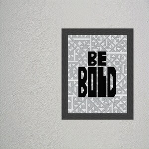 Op de afbeelding: Een zwart-witte ingelijste print met een geometrische achtergrond. De tekst "BE BOLD" is in zwart op de print gedrukt.