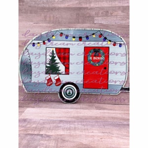 Puede incluir: Una caravana gris y roja con un &aacute;rbol de Navidad, calcetines y una corona en la puerta. La corona tiene un lazo rojo y el texto "The Guzmans" en ella.