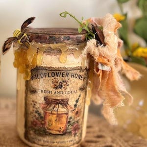 May include: A vintage-style jar of wildflower honey with a decorative label featuring a bee and the text "Wildflower Honey Fresh and Local." The jar is adorned with a fabric bee and dripping honey.