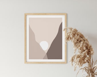 May include: A framed abstract print of a mountain range with a white sun in the center, hanging on a white wall above a wooden cabinet with a vase of dried pampas grass.