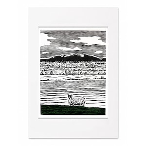 May include: Black and white landscape print featuring a sheep in a field, with a mountain range in the background. The artwork is framed in a white mat. The print depicts a rural scene with a detailed, textured style.