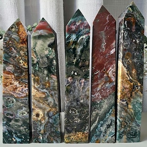 May include: Five polished crystal towers with pointed tops, featuring a complex mix of earthy colors including deep forest green, rusty red, ochre, and cream. Each stone displays unique natural patterns, swirls, and small mineral inclusions.